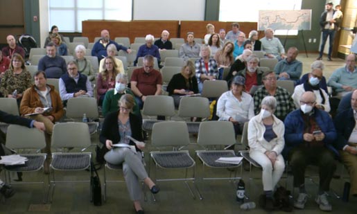 A large-sized conference room where 40-50 members of the community are in attendance, seated and awaiting the start of the presentation.